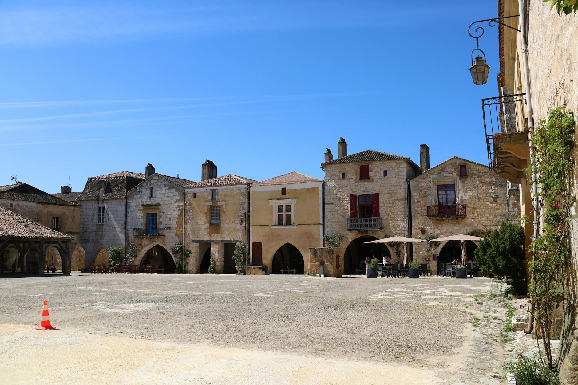 Place de village médiéval français avec arcades et terrasses