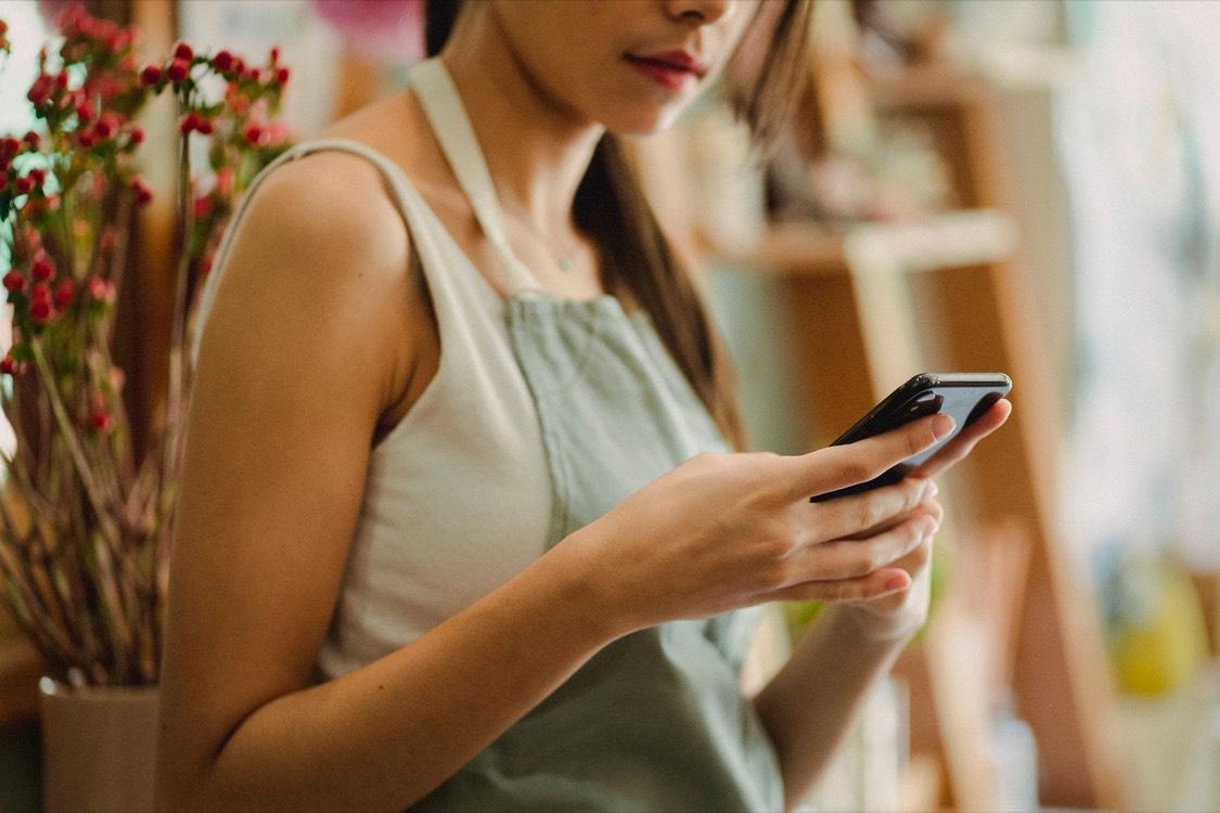 Commerçante en tablier consultant son smartphone dans sa boutique