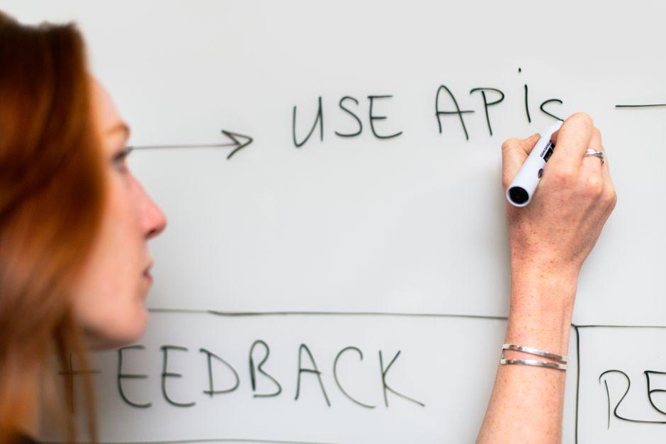 Une femme écrit "Use APIs" sur un tableau blanc, illustrant la planification et la stratégie logicielle
