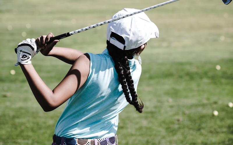 Golfeuse en polo turquoise effectuant un swing sur le practice